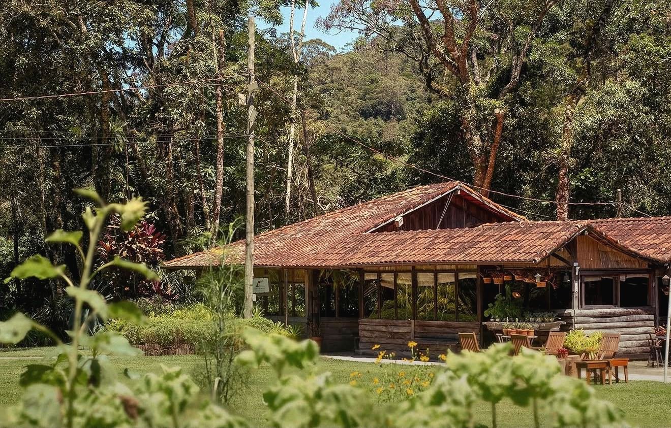 Salão de madeira com telhado de barro do Trilhas do Araçari entre as árvores da Mata Atlântica, em Mury, Nova Friburgo