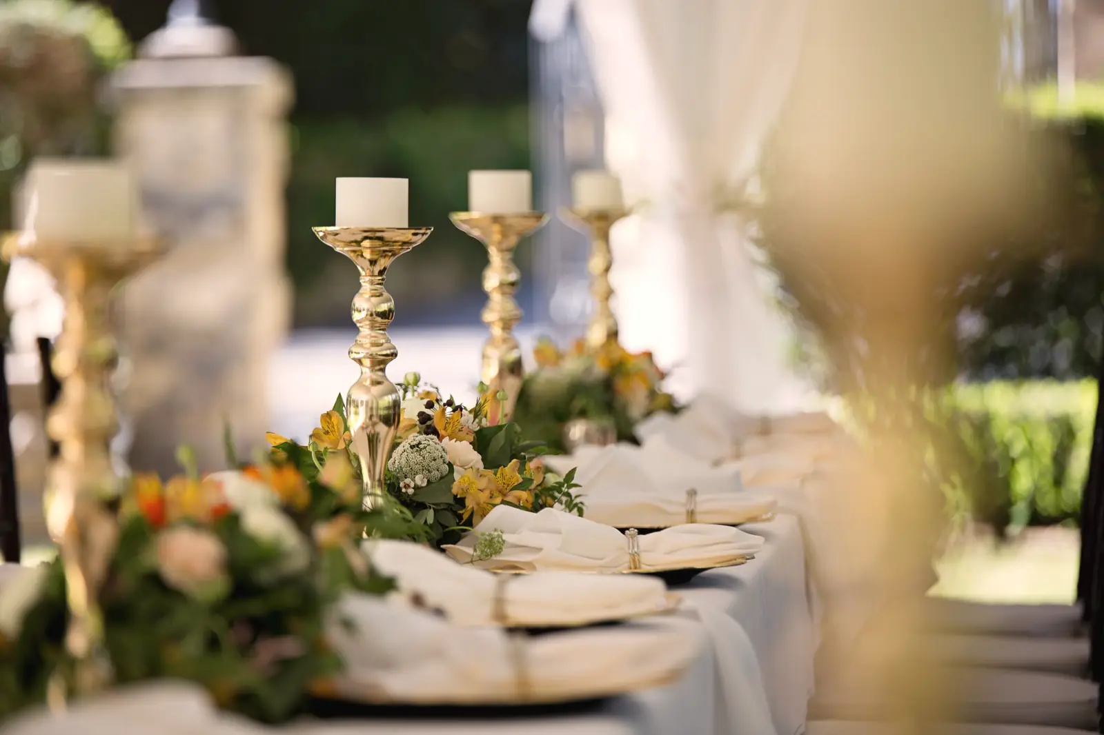 Mesa de casamento posta com castiçais dourados, flores e pratos brancos