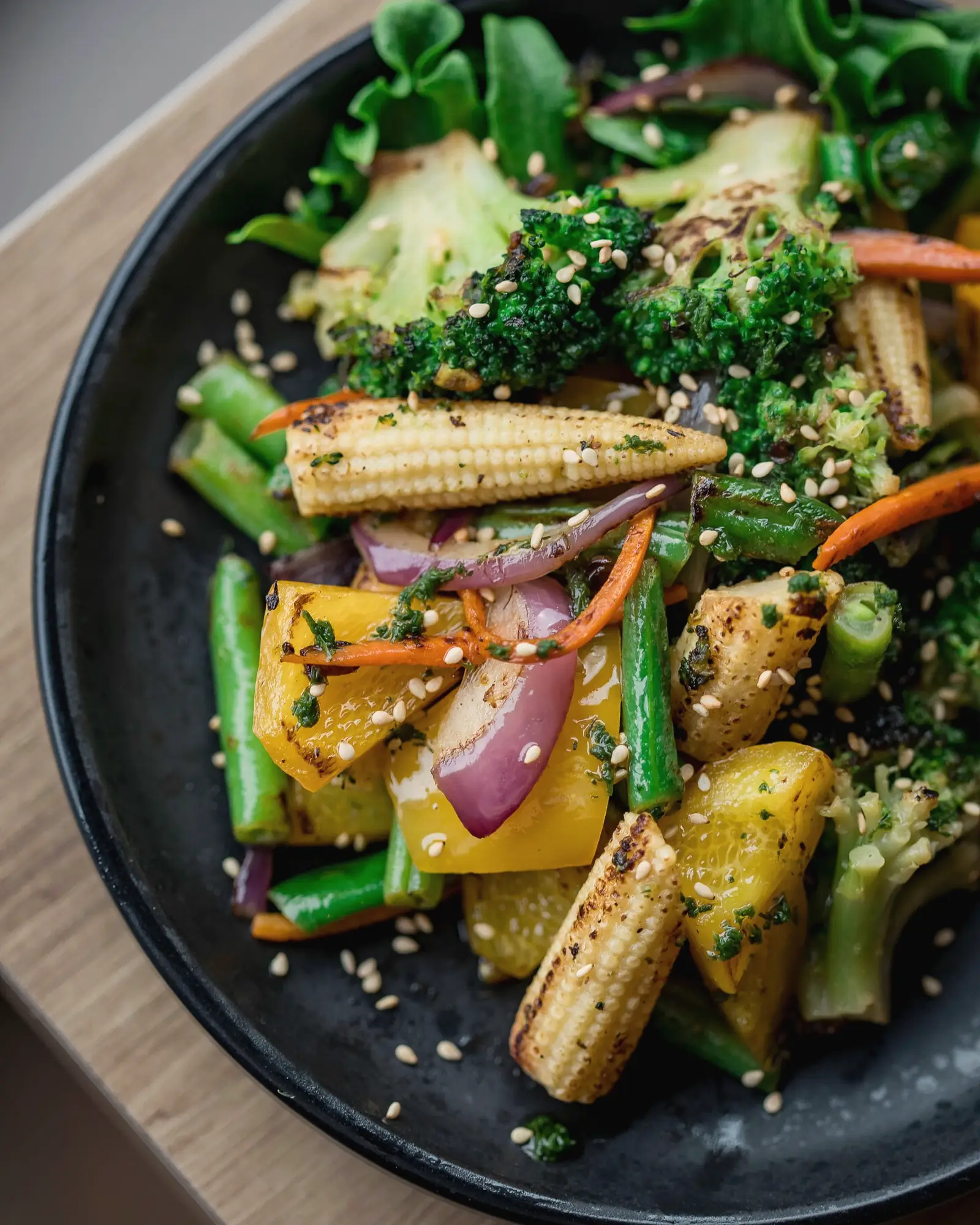 Prato escuro com legumes grelhados coloridos, minimilho, pimentões e brócolis